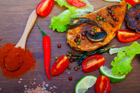 wood fired hoven cooked chicken breast on wood board with herbs spices and vegetablesの写真素材