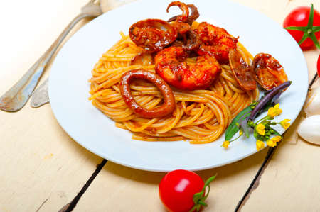Italian seafood spaghetti pasta on red tomato sauce over white rustic wood tableの写真素材