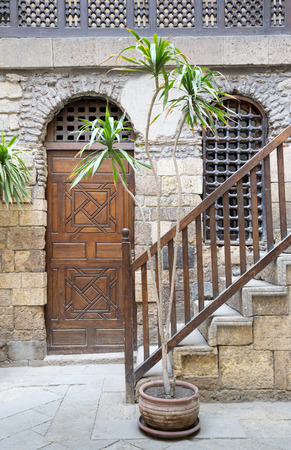 View of the courtyard of Beit El Set Waseela (Waseela Hanem House), showing a wooden closed door and window with interleaved wooden grid and stair with wooden handrail leading to the upper floor, Medieval Cairo, Egyptのeditorial素材