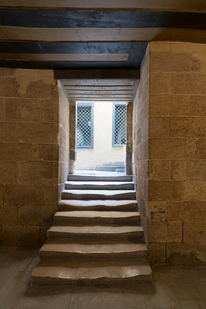 Aged narrow dark vaulted passage and staircase leading to outdoor small lobby with two yellow wooden windows, Medieval Cairo, Egyptのeditorial素材