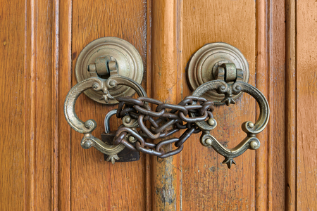 Closeup of two antique copper ornate door knockers over an aged wooden ornate door closed with...