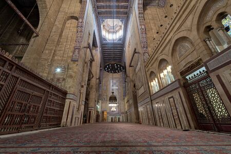 Cairo, Egypt - December 16 2017: Interior of al Refai mosque with old decorated bricks stone wall, colored marble decorations, wooden ornate ceiling, big brass chandeliers, and wooden latticework doorのeditorial素材