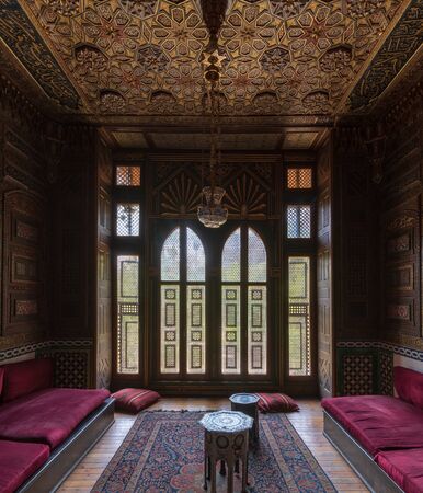 Historic Manial Palace of Prince Mohammed Ali. Small room at reception hall with ornate wooden wall and ceiling, decorated wooden windows, lantern and wooden floor, Cairo, Egyptのeditorial素材