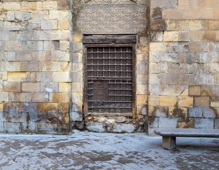Wooden window with decorated iron grid over stone bricks wall and marble garden bench, Moez Street, Cairo, Egyptの写真素材