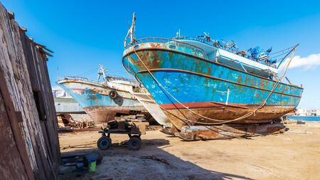 Old rusty vessels under repairing located on grungy dry dock in shipyard against blue sky on sunny day in old shipbuilding plantの写真素材