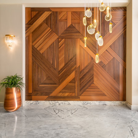 Hall with wood cladding wall decorated with geometrical patterns, tall rounded wooden planter with green bushes, contemporary glass LED tall chandelier, and white marble floor in modern houseの写真素材