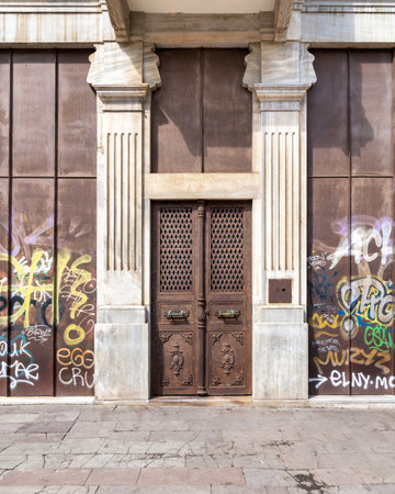 Exterior shot of grunge rusted metal door mediating two marble columns in an abandoned building on city streetの写真素材