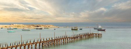 Abandoned ruined fishing pier by the sea in Alexandria, Egypt, with colorful fishing boats in the far end. The pier is framed by the azure waters of the Mediterranean Sea after sunriseの写真素材