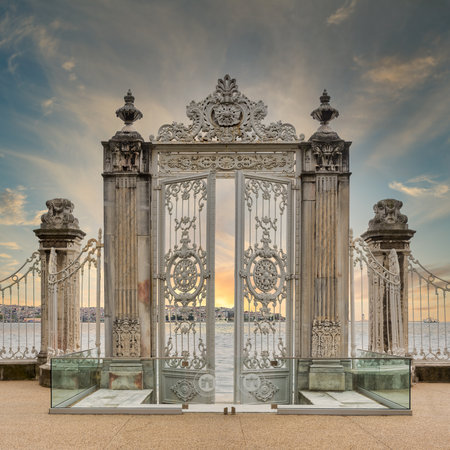 Sunrise shot of pair of half closed elaborately decorated white painted metal gates leading to the...