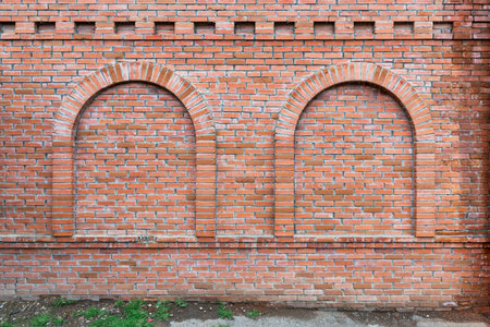 The brick wall features two distinct arched openings, showcasing a textured red surface against a...