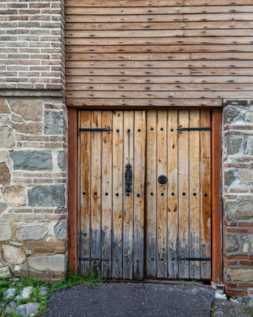 The sturdy wooden door features intricate iron details, set against a weathered stone wall, suggesting a rich history in this quaint area. Lush grass and soft shadows enhance the scenes charmの写真素材