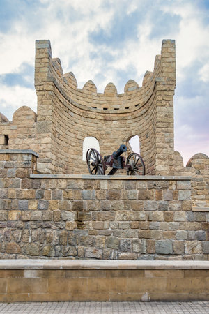Historical fortification in the old city of Baku, Azerbaijan, Icherisheher, showcases a section of the citys ancient stone walls, featuring a cannon, mounted on wheels, rests atop the wallの写真素材
