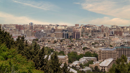 A panoramic view of Baku, Azerbaijan, showcases the contrast between modern skyscrapers and historic buildings in the foreground. Lush greenery envelops the hills, enhancing the scenic beautyの写真素材