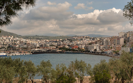 Picturesque view of Kusadasi, Aydin Province, in Turkey showcasing the waterfront and cityscape. Green trees frame the foreground, while the vibrant buildings extend along the coastの写真素材