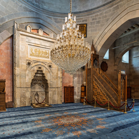 The stunning interior of Kayseri Grand Mosque, Turkish: Ulu Camii, in Kayseri, Turkey. Featuring the ornate mihrab, intricately carved minbar, and grand crystal chandelier above patterned blue carpetの写真素材