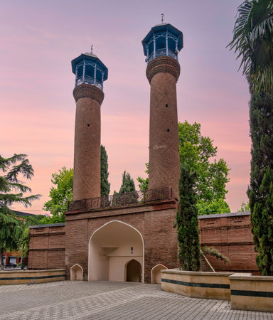 Minarets of Juma Mosque, Ganja, Azerbaijan. Twin brick minarets with blue balconies and crescent moons under a pink sky, surrounded by green treesの写真素材