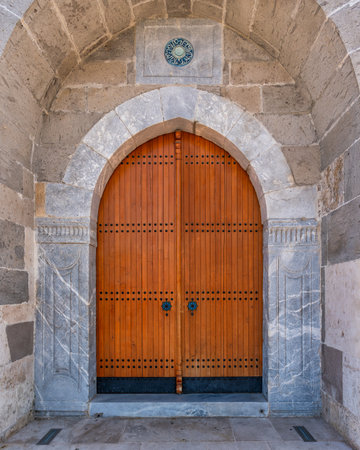 Historic ornate wooden door with arched stone entrance and Arabic calligraphy tile at Alaeddin Mosque, Konya, Turkeyの写真素材