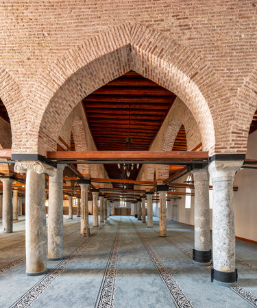 Alaeddin Mosque interior, Konya, Turkey. Rows of ancient stone columns, brick arches, and wooden ceiling above a patterned prayer carpetの写真素材