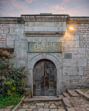 Tomb of Sultan Mustafa Khan III, Istanbul, Turkey. Historic stone entrance with arched wooden door, golden Arabic calligraphy, and evening lightの写真素材