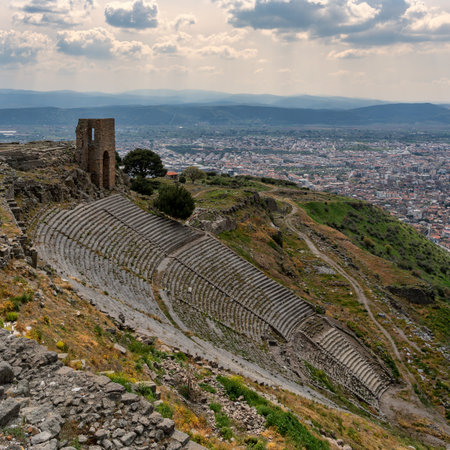 Panoramic view of the steep Ancient Greek Theater of Pergamon ruins, with the city of Bergama, Turkey, and distant mountains under a cloudy sky.の写真素材