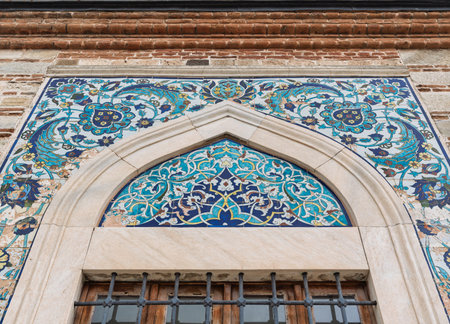 Exterior of Konak Mosque, Izmir, Turkey. Close-up of Iznik blue and turquoise floral tilework above a barred window, set within an arched frame and brick wallの写真素材