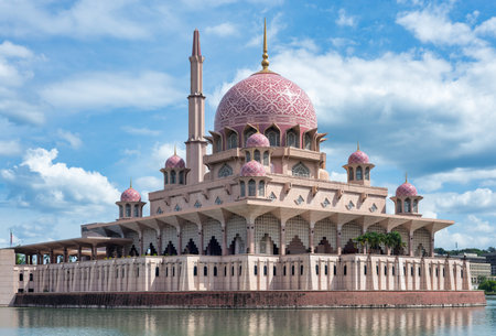 Putra Mosque, Putrajaya, Malaysia. Stunning pink mosque with a grand dome and minaret, reflected in the tranquil water under a bright blue sky with white clouds.の写真素材