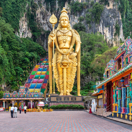 Kuala Lumpur, Malaysia - Feb. 18, 2025: Golden Lord Murugan statue, vibrant rainbow stairs, and ornate temple structures at Batu Caves. Lush green cliffs and peopleのeditorial素材
