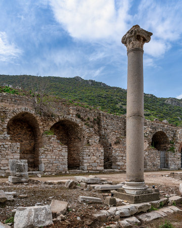 Ancient column with Corinthian capital and stone ruins at the Ancient City of Ephesus, Selcuk, Turkey. Historic archaeological site under a cloudy blue sky.の写真素材
