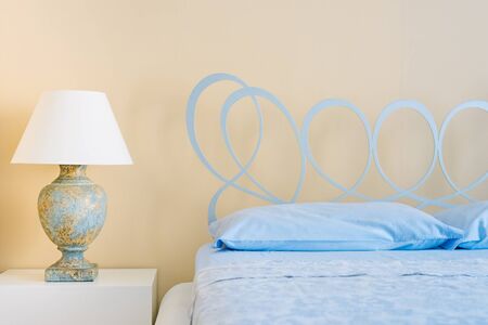 Large comfortable bed with wrought-iron headboard and lamp in a stylish room interior. close- upの写真素材