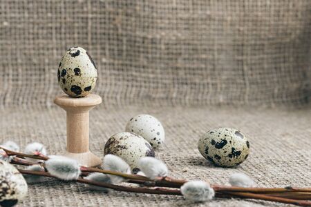 Composition of Easter eggs on a background of rough canvas. Egg on a wooden stand and willow...