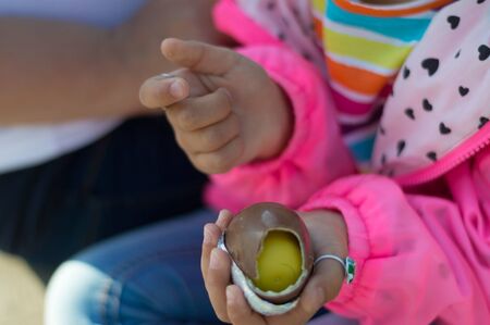 Hands of a girl in a bright rainbow T-shirt are holding a bitten chocolate kinder surprise....