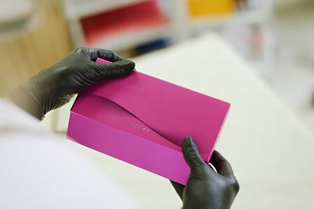 A beautician doctor in black latex gloves holds a closed box with ampoules of filler injection  for...