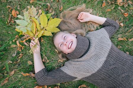 Portrait of a happy beautiful girl holding a bunch of fallen leaves. Positive woman enjoying a warm...
