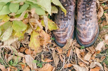 Legs of young woman in rainboots. Woman in gum boots with foliage. Autumn concept