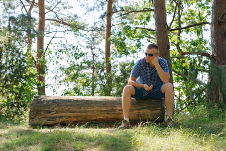 Portrait of a man in the forest. The traveler stopped to rest and sat down in a place for resting tourists near the roadの写真素材