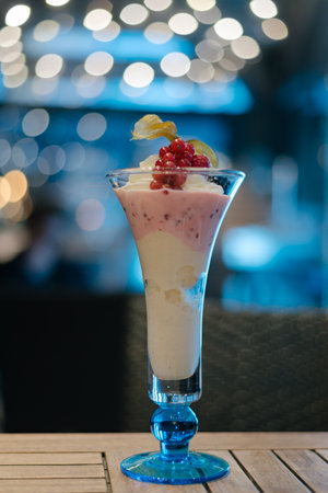 Ice cream with small fruit in a glass on an old wooden bar counter with a bokeh of festive party lightsの写真素材