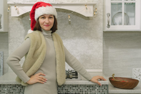 Happy cute woman in santa claus hat smiling and posing in cozy kitchenの写真素材