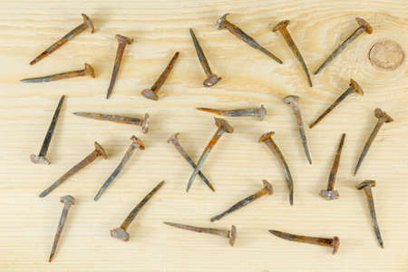 It is a lot of the small old hand-forged nails which are chaotically scattered on a pine board.の写真素材