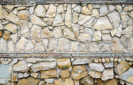 Stone fence. The stone wall is made partially from natural stone, partly of artificial material - brick and tile.の写真素材