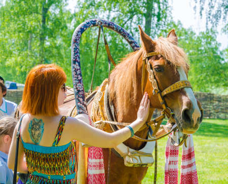 Kazan, Republic of Tatarstan, Russia - May 28, 2016: Red-haired girl petting a horse with red mane. Sabantuy (translated from Tatar - feast of the plow) is a traditional celebration of the end of spring field work.のeditorial素材
