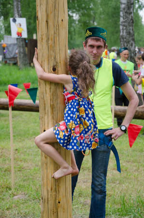 Kazan, Republic of Tatarstan, Russia - May 28, 2016: Girl climbs on a wooden post. Sabantuy (translated from Tatar - feast of the plow) is a traditional celebration of the end of spring field work.のeditorial素材