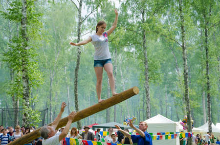 Kazan, Republic of Tatarstan, Russia - May 28, 2016: The young girl balancing goes on a swinging long log. Sabantuy (translated from Tatar - feast of the plow) is a traditional celebration of the end of spring field work.のeditorial素材