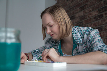 Female artist with blond hair draws in the roomの写真素材