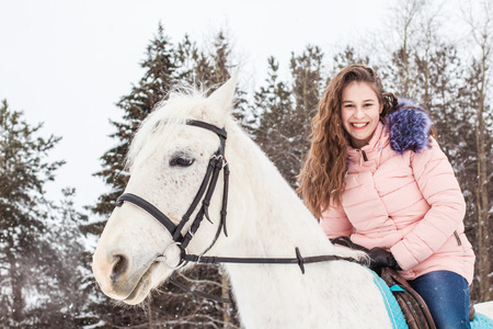 Nice girl and white horse outdoor in snowfall in a winter dayの写真素材