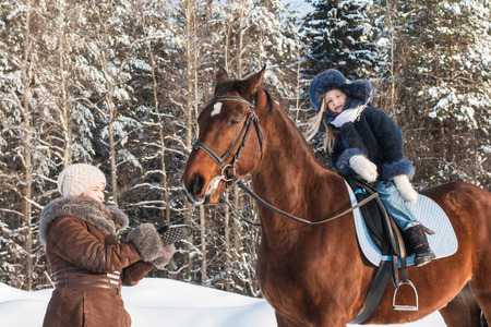 Small girl and mom near horse in a winter dayの写真素材