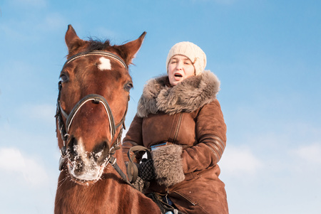 Woman in brown dress and brown horse in a winter dayの写真素材