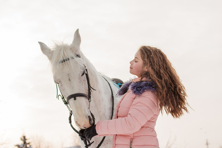 Nice girl and white horse outdoor in snowfall in a winter dayの写真素材
