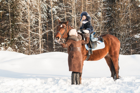 Small girl and mom near horse in a winter dayの写真素材