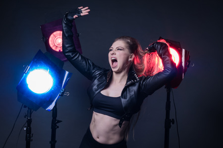 Girl in a leather jacket on stage and three colored spotlightsの写真素材