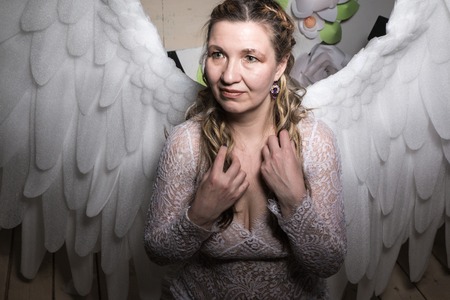 Ugly woman in a white dress with white wings is trying to look as angelの写真素材